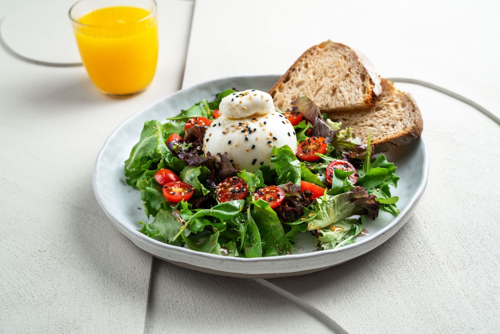 Queso burrata sobre verduras mixtas con tomates cherry y rebanadas de pan