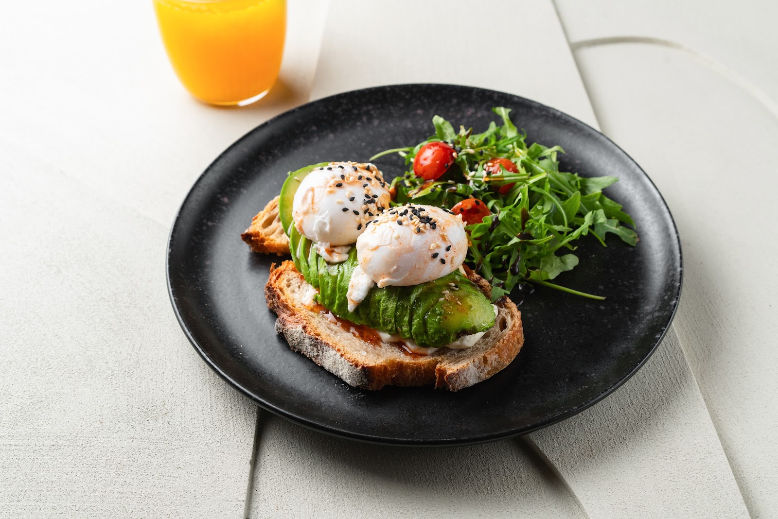 Huevos poché sobre tostada de aguacate con rúcula y tomates cherry en plato negro